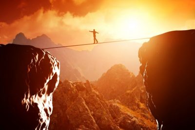 Man walking a tight rope between two mountains as the Global economy tries to balance